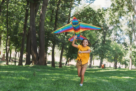beautiful happy child holding colorful kite and running in parkの写真素材