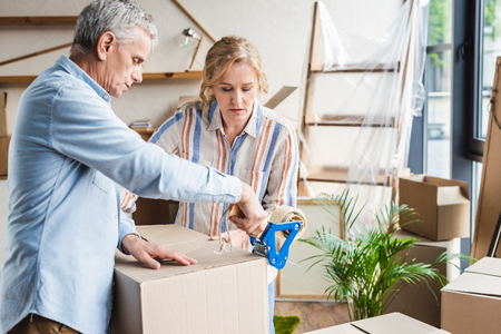 focused senior couple packing cardboard boxes while moving homeの写真素材