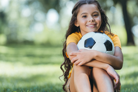 adorable happy child holding soccer ball and smiling at camera in parkの写真素材