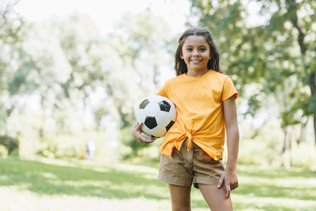 beautiful happy kid holding soccer ball and smiling at camera in parkの写真素材