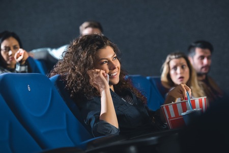 smiling woman talking on smartphone while watching movie in cinemaの写真素材