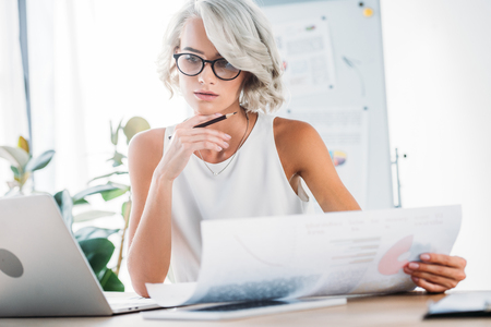 beautiful caucasian businesswoman working in office with documents and laptopの写真素材