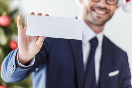 cropped image of businessman holding blank card in office with blurred christmas tree on backgroundの写真素材