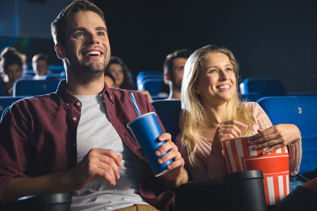 cheerful couple with popcorn and soda drink watching film together in cinemaの写真素材