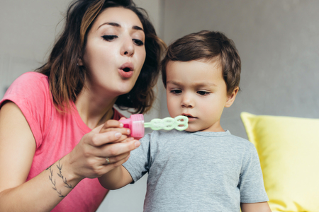 mother and little son blowing soap bubbles together at home