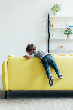 little boy climbing up on yellow sofa at homeの写真素材