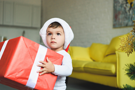 adorable boy in santa hat holding big red christmas presentの写真素材