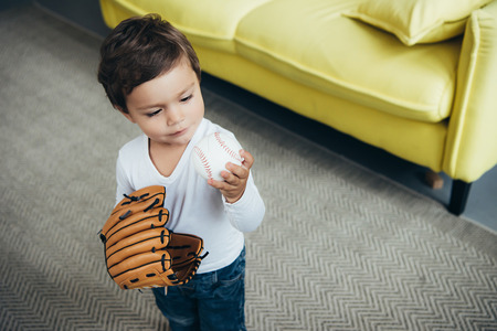 adorable little child playing with baseball glove and ball at homeの写真素材