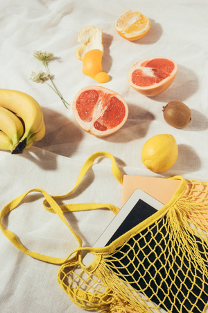 tablet computer in yellow string bag and fresh ripe tropical fruitsの写真素材