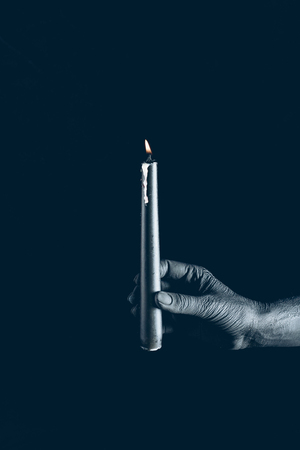 partial view of demon holding flaming candle in black hand, isolated on blackの写真素材