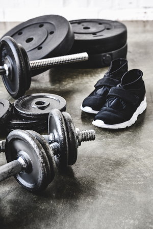 close-up shot of dumbbells and barbell with weight plates and sneakers on concrete floorの写真素材