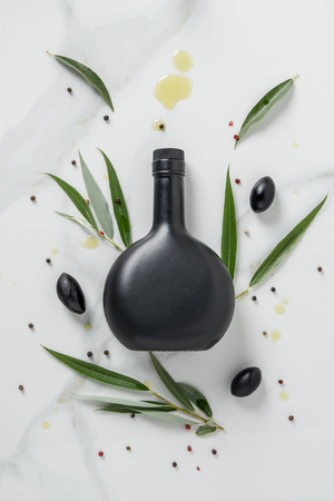 elevated view of black bottle of olive oil and olives on marble tableの写真素材