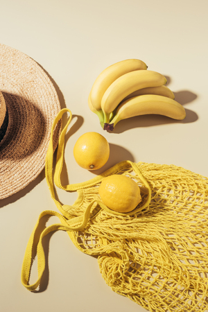 top view of straw hat and yellow string bag with lemons and bananasの写真素材