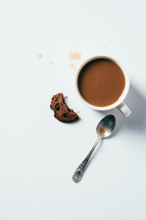 top view of cup of coffee with bitten chocolate chip cookie and spoon on white surfaceの写真素材