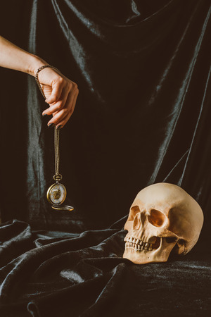 cropped view of woman holding vintage clock on the chain near skull on black clothの写真素材