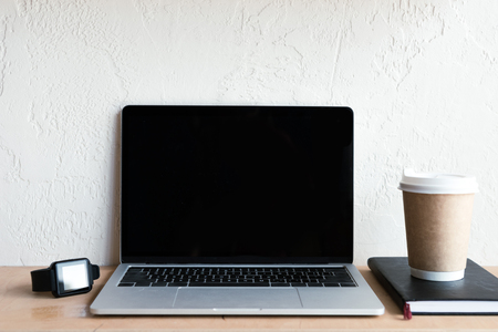 laptop with blank screen, smartwatch, notebook and coffee to go on tableの写真素材