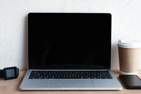 laptop with blank screen, smartwatch, smartphone and coffee to go on tableの写真素材
