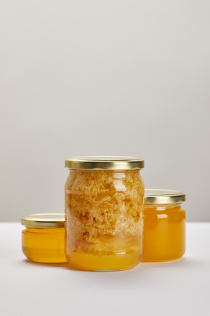 close up view of glass jars with honey on white surface on grey backdropの写真素材