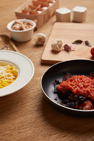 close-up shot of plate of spaghetti and tomato sauce in frying pan on wooden tableの写真素材
