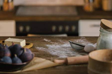 close-up shot of fig pie ingredients standing on wooden table covered with flour