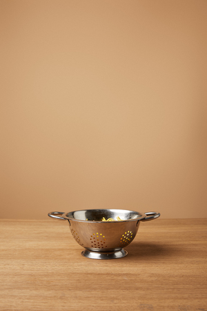 metal colander with spaghetti on wooden table in front of light brown backgroundの写真素材
