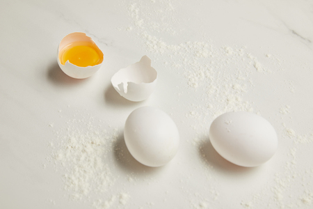 close up view of raw chicken eggs and flour on white marble tabletop
