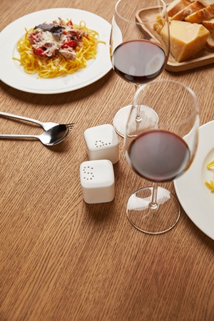 close-up shot of plates of tasty pasta with red wine in glasses on wooden table