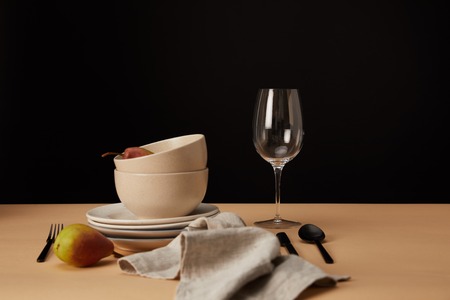 plates, bowls, wineglass, napkin and pears on beige tableの写真素材