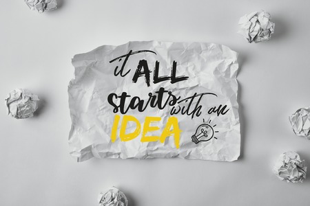top view of damaged paper with "it all starts with an idea" inspiration surrounded with crumpled papers on white surfaceの写真素材