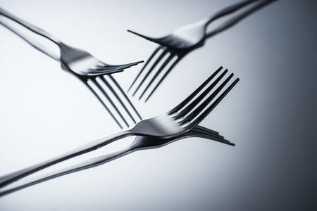 close-up view of three shiny forks reflected on greyの写真素材