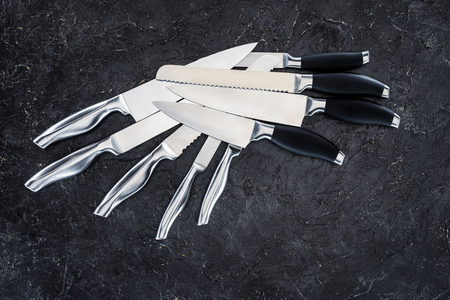set of various kitchen knives arranged on black, top view