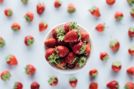 top view of bowl of fresh whole strawberries on white tabletopの写真素材