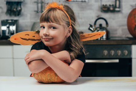 little kid in halloween costume standing at tabletop with pumpkin in kitchen at homeの写真素材