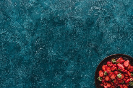 top view of bowl with ripe strawberries on blue concrete surfaceの写真素材