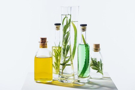 transparent bottles of natural aromatic essential green and yellow oils on white cube