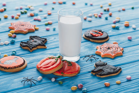 close up view of candies, homemade halloween cookies and glass of milk on wooden tableの写真素材