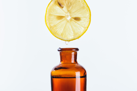 aromatic juice of lemon piece dripping into bottle of natural herbal essential oil isolated on whiteの写真素材