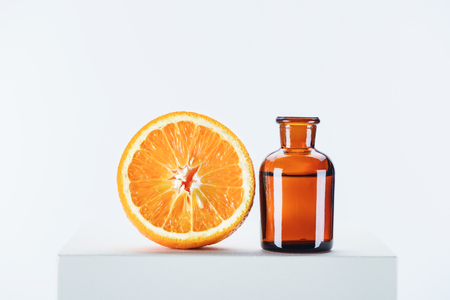 bottle of natural herbal essential oil and cut orange on white cubeの写真素材