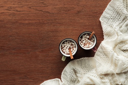 top view of mugs with delicious hot chocolate, marshmallows and cinnamon sticks on wooden backgroundの写真素材