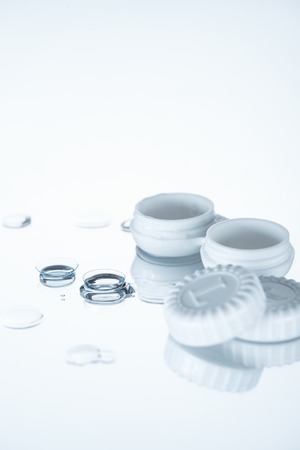 close up view of container and contact lenses on white backdropの写真素材