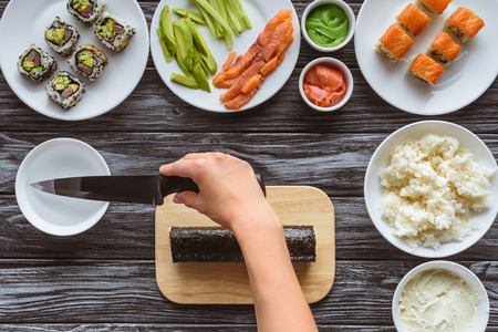 cropped shot of person holding knife and preparing delicious sushi rollの写真素材
