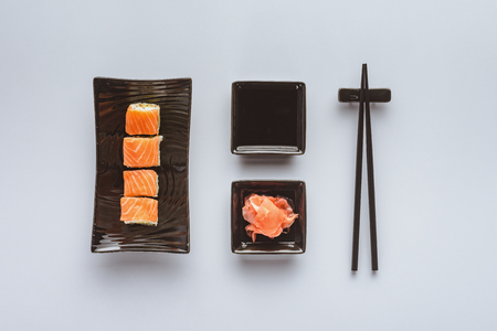 top view of delicious sushi with salmon, ginger, soy sauce and chopsticks isolated on whiteの写真素材