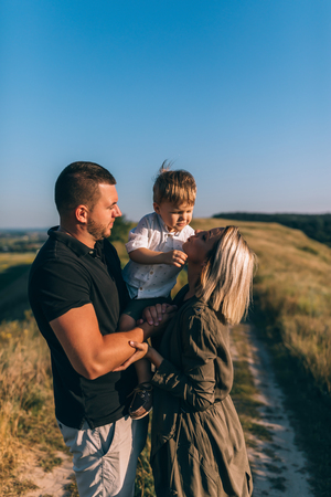 happy young parent carrying adorable little son while standing on rural pathの写真素材