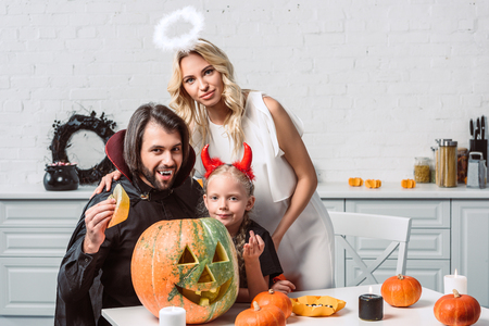 portrait of family in halloween costumes at table with pumpkins in kitchen at homeの写真素材