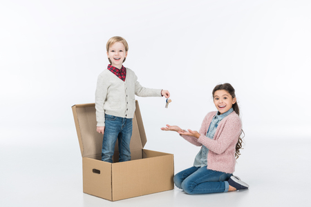 Little boy giving key from new house to surprised sister ready to move into new house isolated on whiteの写真素材