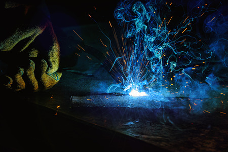 partial view of worker welding metal with sparks at factory