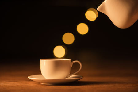 close up view of white jug, cup of coffee and bokeh lights on black backdropの写真素材