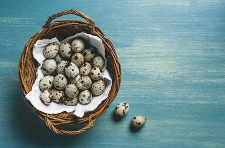 top view of raw healthy quail eggs in wicker basket on turquoise wooden tableの写真素材