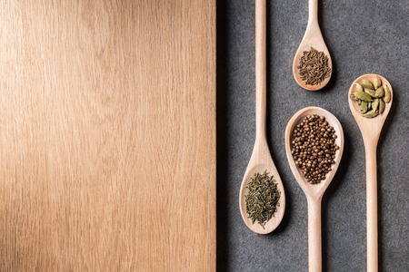 top view of dried spices on wooden spoons and wooden board on grey backgroundの写真素材