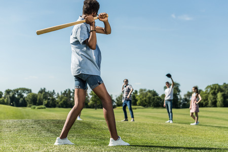 african american teenager holding baseball bat and playing with friends in parkの写真素材